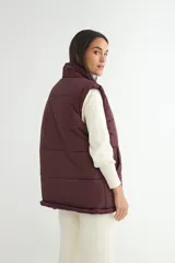 Chaleco acolchado color chocolate con interior y cuello de corderito sintético. Presenta cierre frontal con botones a presión y bolsillos laterales.