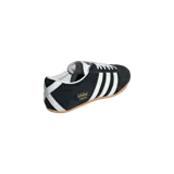 Championes Adidas Tokyo Core Black confeccionados en gamuza negra, con las tres franjas características en blanco y suela de goma marrón. Incluye la inscripción "Tokyo" en letras doradas al costado.