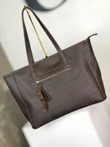Bolso tipo shopper de cuero marrón chocolate, con doble asa de hombro, cierre superior y bolsillo frontal con cierre y tirador decorativo de cuero con estampa animal print.