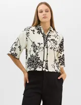 Camisa de corte holgado con estampado botánico en blanco y negro. Presenta cuello camisero, mangas cortas amplias y cierre frontal con botones y vivos a contratono.