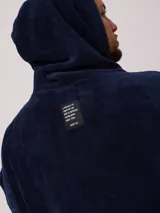 Poncho de toalla con capucha en color azul marino, confeccionado en 100% algodón. Presenta un bordado blanco del logo de Rusty en el pecho.