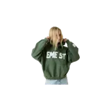 Hoodie oversize de Eme Studios modelo Class 3A Forest, color verde militar con capucha y bolsillo tipo canguro. Presenta un estampado frontal con letras grandes en color blanco y una etiqueta decorativa en el puño.