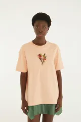Remera oversize color salmón, de manga corta y cuello redondo, con pequeño bordado floral en el centro del pecho.