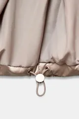 Anorak acolchado de efecto brillante con tejido cortavientos y repelente al agua. Presenta cuello subido, cierre frontal con cremallera, bolsillos delanteros con forro polar y cierre de cremallera, y mangas largas con puños elásticos. El bajo es ajustable con cordones elásticos laterales.