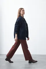 Pantalón de fit recto color beige, confeccionado en cotton spandex. Presenta costuras visibles y bordados decorativos en tono dorado/marrón claro. El ruedo del pantalón tiene un borde festoneado.