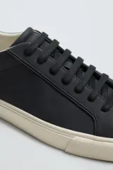 Zapatilla de cordones color negro con parte superior lisa, horma redonda y forro interior a contraste. Suela de goma color crema con ligera textura y detalle en el talón color crema.