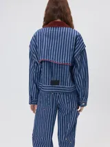 Campera de denim a rayas verticales con cuello de pana en color bordó. Presenta cierre frontal, mangas desmontables con cierre en los hombros, canesú en el pecho y bolsillos de parche cuadrados.