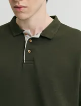 Remera de manga larga con cuello polo, confeccionada en tejido de punto canalé francés. Presenta abotonadura frontal con botones de madera y detalles a contratono en la cartera y el interior del cuello.