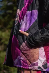 Chaqueta negra con estampado de hojas en tonos rosa, violeta y marrón. Diseño acolchado con cuello clásico y cierre frontal con botones.