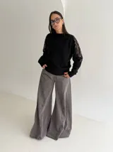 Sweater negro de tejido de punto con cuello redondo y mangas largas. Presenta detalles de transparencias y apliques bordados con pedrería en la parte superior de las mangas.