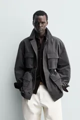 Cazadora relaxed fit de hombre, confeccionada en tejido técnico con algodón de color negro. Cuenta con cuello camisero, manga larga y bolsillos frontales de plastrón con solapa. Presenta cintura ajustable con cordón interior y cierre frontal con cremallera oculta por solapa con botones a presión.