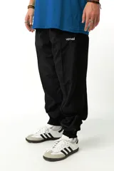 Pantalón de jogging negro de nylon con forro interno de red, corte recto, bolsillos laterales con cierre, cierres en los tobillos y cintura elástica con cordón ajustable.