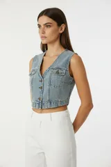 Chaleco corto de jean celeste lavado, con escote en V, botones frontales y bolsillos superiores con tapa.
