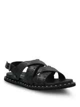 Sandalias negras de cuero con diseño de tiras cruzadas, decoradas con tachas metálicas. Poseen ajuste mediante hebilla lateral y suela de goma con detalle de tachas en el borde.