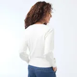 Sweater de punto color blanco con diseño cruzado tipo cárdigan, escote en V profundo y cierre lateral con un botón dorado. Presenta mangas largas con puños ajustados y un corte entallado a la cintura.