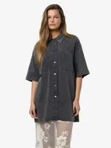 Vestido camisero corto de denim negro con lavado ácido, manga corta, cierre frontal con botones, dos bolsillos con solapa en el pecho y corte holgado.