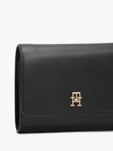 Billetera trifold de Tommy Hilfiger en color negro, confeccionada en poliuretano con acabado texturizado. Presenta un diseño plegable con solapa frontal y el logo metálico TH en tono dorado en el centro.