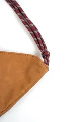 Cartera tipo hobo de gamuza color marrón, con costura central vertical y correa de cuerda trenzada en tonos borró y gris con nudos decorativos en los extremos.