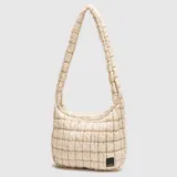 Tote bag de diseño acolchado y voluminoso, color beige, con correa de hombro integrada y cierre superior. Presenta una etiqueta pequeña con el logo de la marca en la parte inferior.