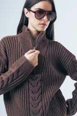 Sweater de punto grueso color azul marino, con cuello polo y cierre frontal parcial. Presenta un diseño de tejido trenzado en el centro y mangas largas con puños acanalados.