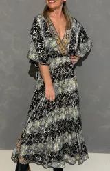 Vestido largo cruzado al frente de seda estampado en tonos azules, negros y dorados, con escote en V ribeteado, mangas 3/4 fluidas y elástico en la parte trasera de la cintura.