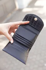 Billetera pequeña negra de cuero con textura tipo cocodrilo y cierre con broche. Hecha a mano en Uruguay.