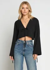 Top negro de corte cropped con escote en V profundo y cierre frontal mediante lazo anudable. Presenta mangas largas acampanadas con detalle de lazos en los puños.