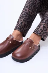 Zueco de cuero sintético color beige, con interior forrado en corderito sintético, tira ajustable con hebilla metálica y suela de goma negra con plataforma dentada.