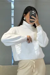 Buzo de chenille color blanco, con cuello alto tipo polera, mangas largas con puños ajustados y diseño de tejido acanalado.