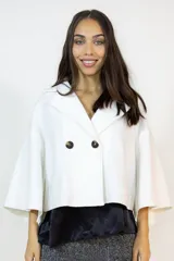 Capa corta de paño en color blanco, con diseño de doble botonadura frontal y cuello solapa. Presenta mangas amplias y corte holgado que aporta movimiento y sofisticación.