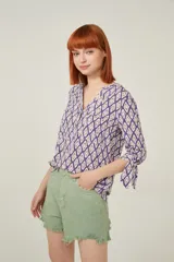 Blusa de viscosa con estampado geométrico en tonos violeta y beige. Tiene cuello mao, botones frontales y mangas 3/4 con lazo en los puños.
