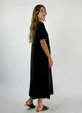 Vestido midi dorado con brillo, escote en V con ribete blanco y mangas cortas con puños blancos. Tiene aberturas laterales en el ruedo.