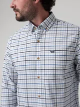 Camisa de franela de algodón orgánico para hombre, con diseño de cuadros en tonos celestes, azules y oscuros sobre base blanca. Presenta cuello abotonado, cierre frontal de botones, bolsillo aplicado en el pecho y un pequeño bordado distintivo de la marca RKF.