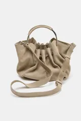 Bolso tipo saca de serraje color beige con doble asa rígida asimétrica y asa bandolera extraíble. Incluye cartera con bolsillo extraíble.