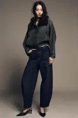 Jeans de tiro alto con corte barrel y diseño tapered, confeccionados en denim con efecto lavado y detalle de raya planchada. Presentan cintura con trabillas, cierre frontal con cremallera y botón, y bolsillos funcionales en delantero y espalda.