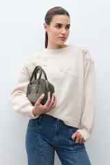 Sweater de punto en color beige melange, con cuello redondo y mangas largas. Presenta apliques de flores tejidas en relieve sobre los hombros y el pecho.
