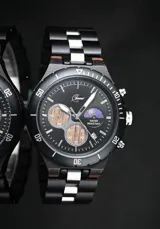 Reloj cronógrafo de la colección Imperial, con caja de madera de ébano oscuro y bisel técnico. La esfera negra presenta subdiales con textura de madera natural, indicador de fase lunar y fechador. La malla combina eslabones de acero inoxidable pulido con madera de ébano, ofreciendo un diseño sofisticado y resistente.