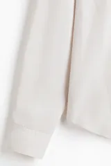 Camisa de vestir color beige claro, de manga larga, con cuello inglés y cierre de botones. Presenta un corte slim fit y bajo ligeramente redondeado.