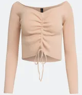 Blusa cropped de punto acanalado color beige, con escote ombro a ombro, manga larga y cordón ajustable con lazo.