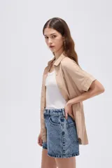 Camisa de viscosa color beige, con cuello camisero, mangas cortas, cierre frontal con botones ocultos y cordón ajustable en la cintura.
