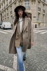 Abrigo largo cruzado color gris oscuro, confeccionado con lana. Presenta cuello solapa, manga larga, bolsillos delanteros de plastrón y cierre frontal con botones.