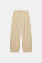 Pantalón de tiro alto en color beige, con pinzas delanteras, bolsillos laterales y bajo con vuelta. Presenta un cierre frontal con cremallera, botón interior y gancho.