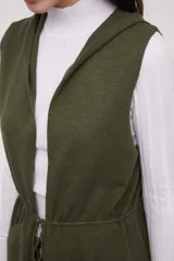 Chaleco largo sin mangas de tejido de punto color negro, con capucha y lazo ajustable en la cintura. Presenta bolsillos frontales y diseño abierto.