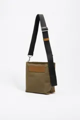 Bolso bandolera de tamaño pequeño en color verde oliva, confeccionado en poliamida con detalles en piel vacuna. Cuenta con asa larga regulable de tejido en color negro, cierre superior con cremallera y logo de la marca estampado en la parte frontal.