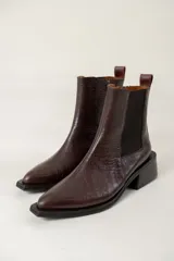 Bota tipo chelsea de caña media con acabado efecto cocodrilo en color chocolate. Presenta paneles elásticos laterales, puntera cuadrada y taco ancho geométrico.