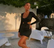 Vestido corto de manga larga en color negro con destellos dorados de lurex. Presenta un diseño ajustado con aberturas laterales en la cintura y escote redondo.