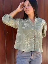 Camisa de corte holgado en color verde con estampado floral lineal en tono crema. Presenta cuello mao, cierre frontal con botones y mangas tres cuartos con puños elásticos.