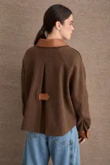 Campera corta de paño color marrón con detalles en cuero sintético al tono en cuello, puños y solapas de bolsillos. Presenta cierre frontal con botones metálicos dorados y dos bolsillos frontales tipo cargo.