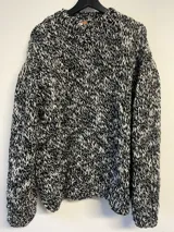 Sweater tejido a mano en lana color gris jaspeado, de calce holgado, con cuello a la base y puños ajustados.