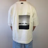 Remera oversize de algodón pesado en color blanco off-white, con un gran estampado fotográfico en blanco y negro en la espalda acompañado de texto.
